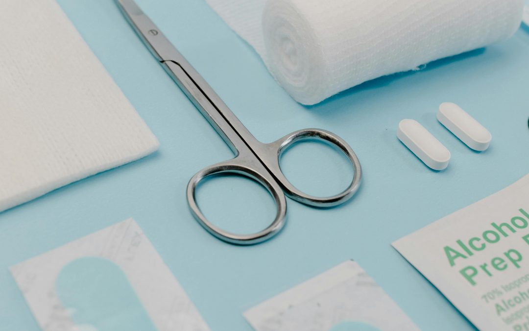 Medical supplies on a blue surface, including scissors, bandages, alcohol prep pads, pills, a mask, and gauze.